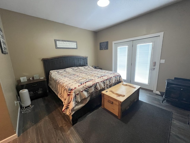 bedroom with dark wood-style floors, baseboards, a wood stove, and access to exterior