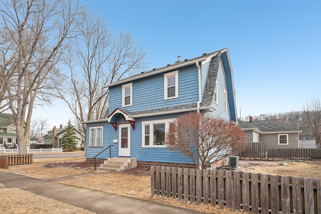 view of front facade with central air condition unit, a fenced front yard, and a gambrel roof