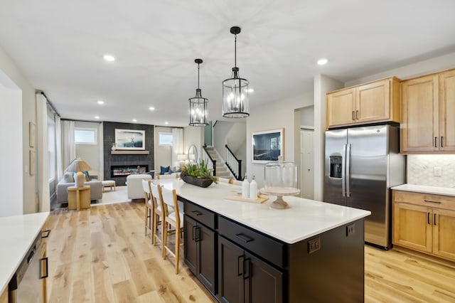 kitchen featuring a large fireplace, open floor plan, stainless steel appliances, light wood-style floors, and light brown cabinets