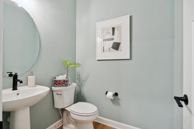 half bath with wood finished floors, a sink, toilet, and baseboards