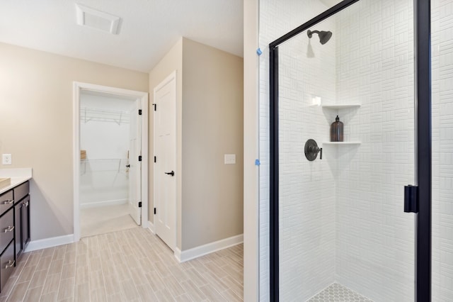 full bathroom with a spacious closet, a stall shower, vanity, and baseboards