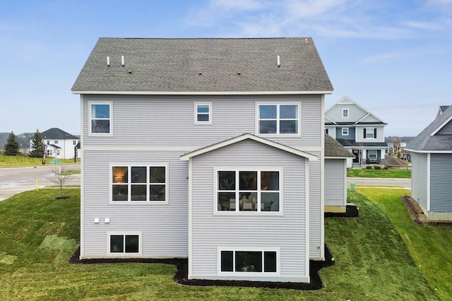 back of property featuring roof with shingles and a yard