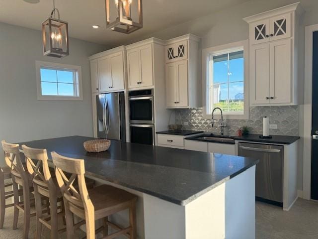 kitchen featuring tasteful backsplash, dark countertops, appliances with stainless steel finishes, white cabinetry, and a sink