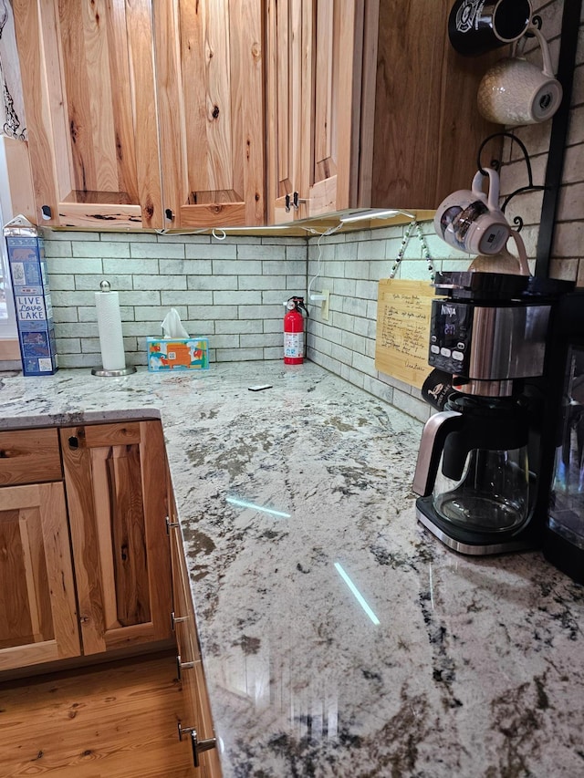 kitchen featuring brown cabinetry, light stone countertops, and decorative backsplash