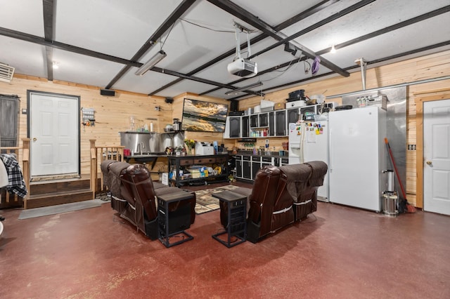 garage with a garage door opener, freestanding refrigerator, and wooden walls