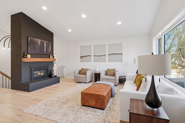 living area with lofted ceiling, a brick fireplace, recessed lighting, and wood finished floors