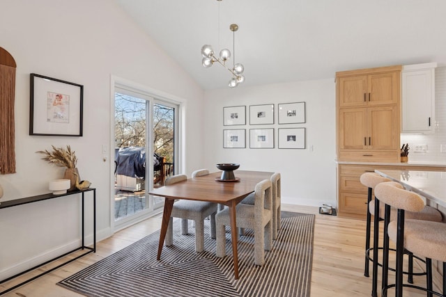 dining area featuring light wood-style floors, vaulted ceiling, baseboards, and an inviting chandelier