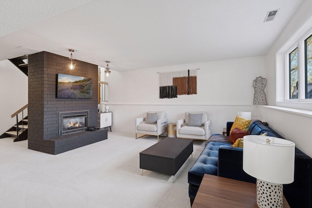 carpeted living area with stairway, a brick fireplace, and visible vents