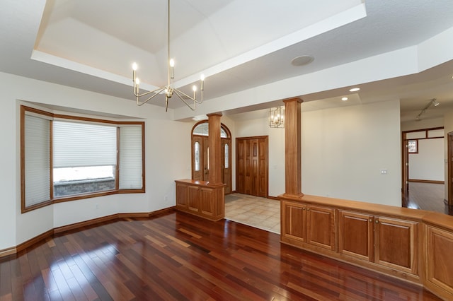 spare room with dark wood finished floors, a raised ceiling, baseboards, and decorative columns