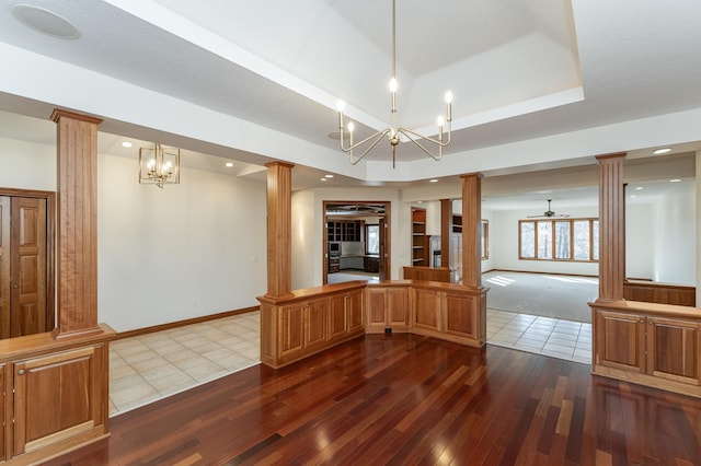 empty room with baseboards, dark wood finished floors, a tray ceiling, decorative columns, and a ceiling fan