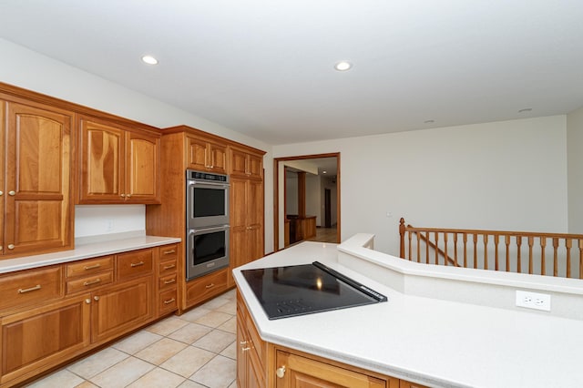 kitchen featuring double oven, brown cabinetry, light countertops, light tile patterned floors, and black electric cooktop