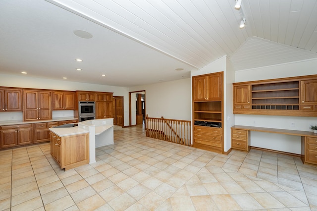 kitchen featuring open shelves, a center island, light countertops, built in study area, and vaulted ceiling