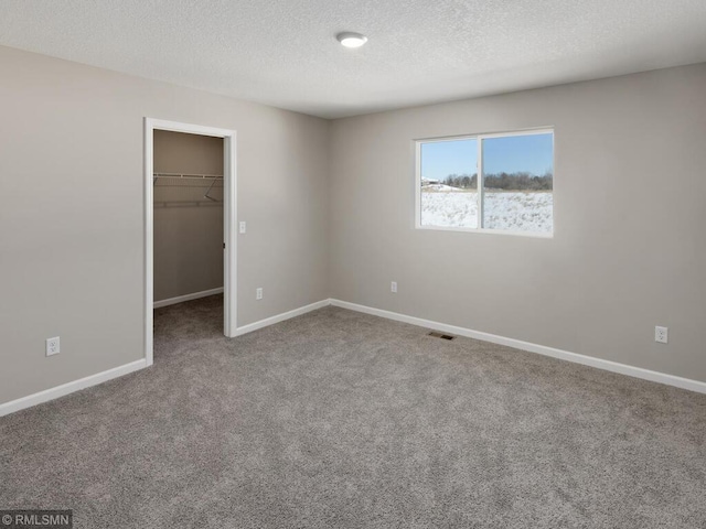 unfurnished bedroom with baseboards, a spacious closet, a textured ceiling, carpet flooring, and a closet