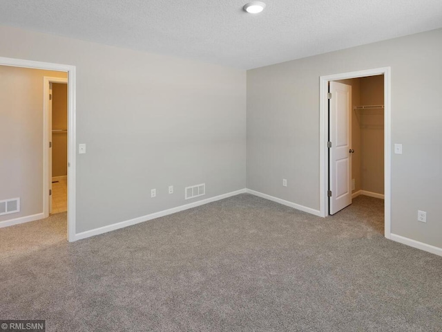 unfurnished bedroom with carpet, a spacious closet, visible vents, and baseboards