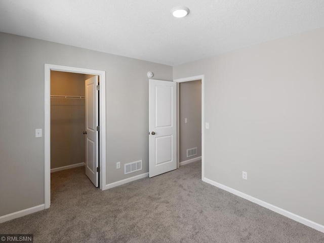 unfurnished bedroom with carpet, a walk in closet, visible vents, and baseboards