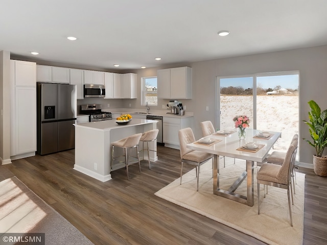 kitchen with dark wood-style flooring, a kitchen island, a sink, white cabinetry, and appliances with stainless steel finishes