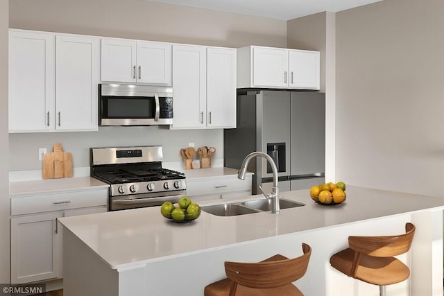 kitchen with a kitchen bar, a sink, white cabinetry, appliances with stainless steel finishes, and light countertops