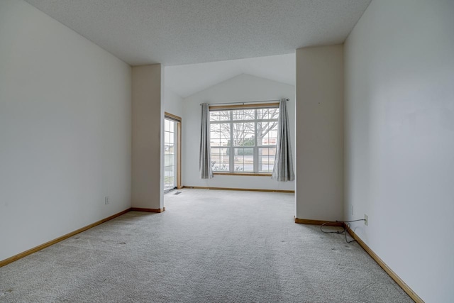 empty room featuring lofted ceiling, a textured ceiling, baseboards, and carpet flooring