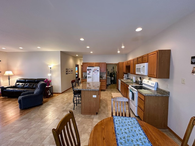 kitchen featuring a breakfast bar, recessed lighting, open floor plan, a sink, and white appliances