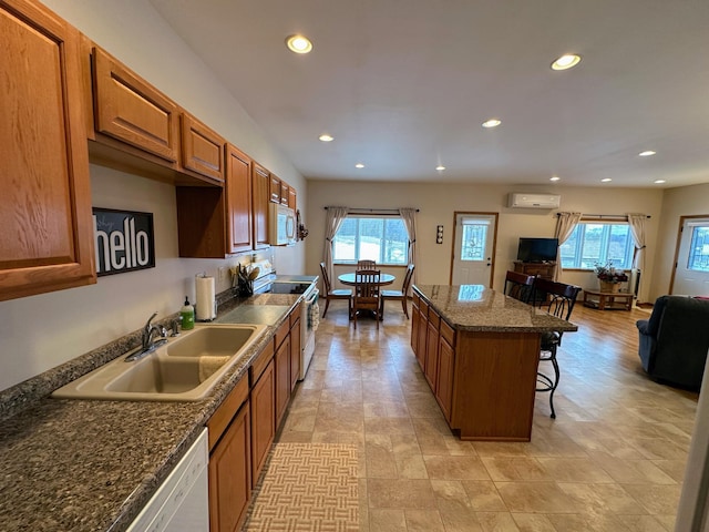 kitchen featuring white appliances, a sink, a center island, a wall mounted AC, and brown cabinets