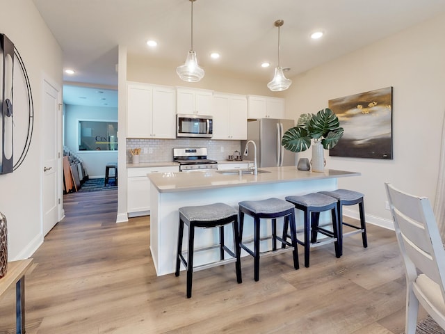 kitchen with stainless steel appliances, backsplash, a sink, and light wood-style flooring