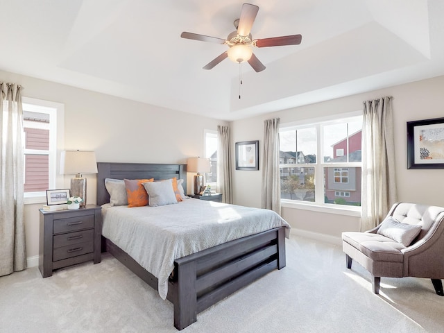 bedroom featuring baseboards, ceiling fan, a tray ceiling, and light colored carpet