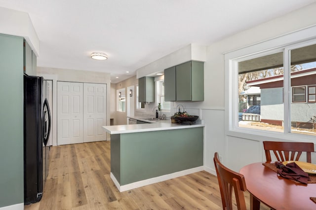 kitchen with light wood-style flooring, a peninsula, a sink, freestanding refrigerator, and green cabinetry