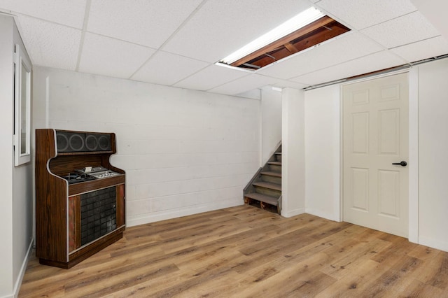 finished below grade area with concrete block wall, a drop ceiling, stairway, and wood finished floors