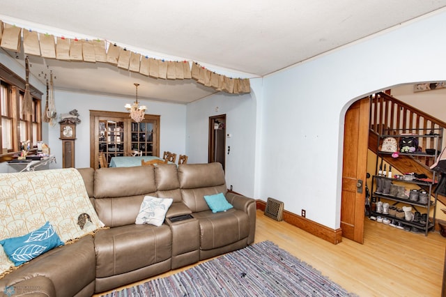 living room featuring arched walkways, baseboards, light wood-style flooring, stairway, and a notable chandelier