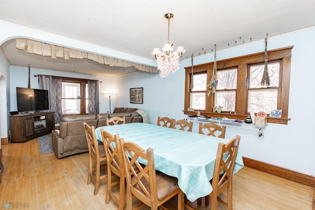 dining room featuring a notable chandelier, light wood-type flooring, arched walkways, and baseboards