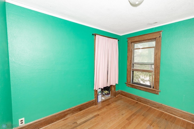 spare room with crown molding, a textured wall, wood finished floors, and baseboards