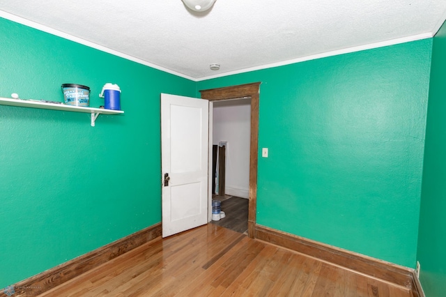 empty room with a textured wall, ornamental molding, a textured ceiling, wood finished floors, and baseboards