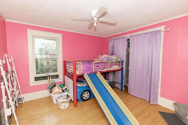 bedroom featuring ornamental molding, a textured ceiling, baseboards, and wood finished floors