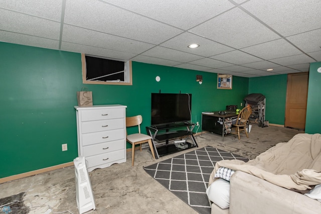 living area with an accent wall, unfinished concrete flooring, a paneled ceiling, and baseboards