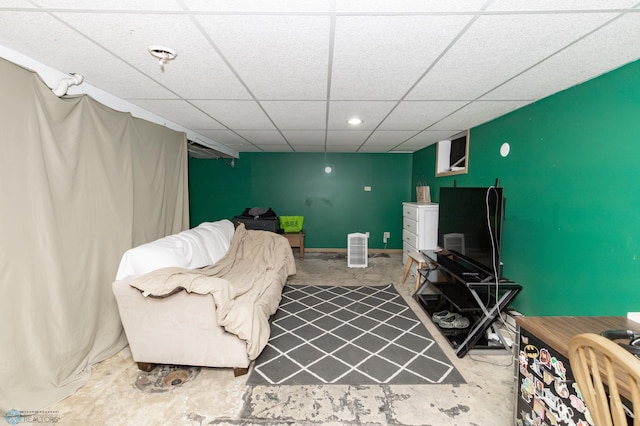 living room with an accent wall, baseboards, concrete flooring, and a drop ceiling