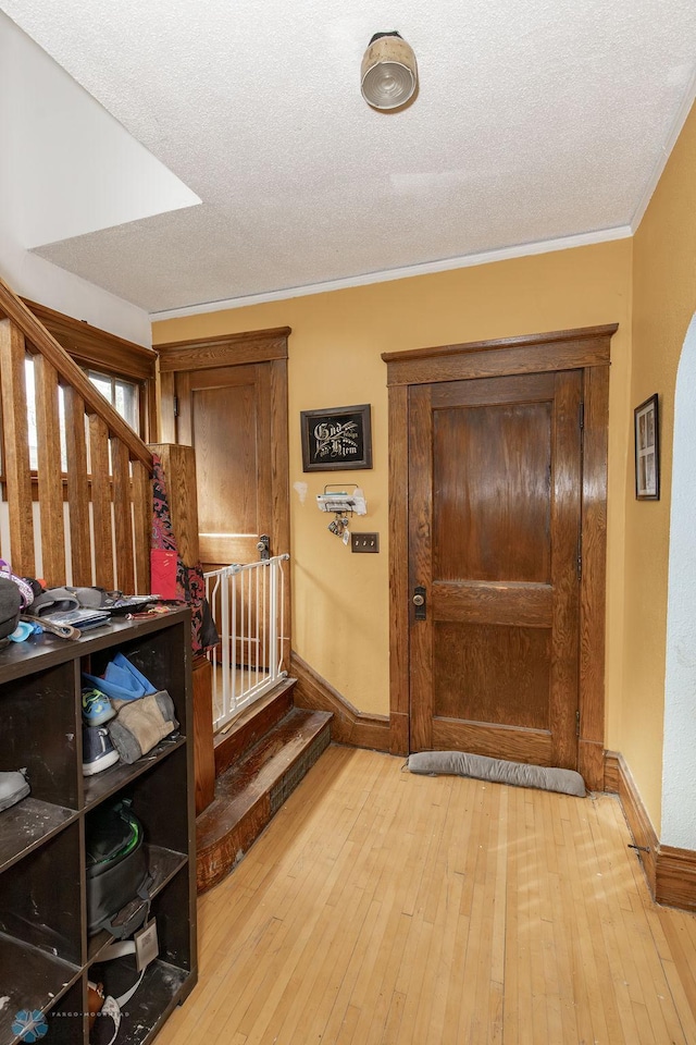 corridor featuring light wood-type flooring, stairway, and a textured ceiling