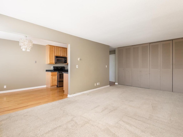 unfurnished living room with a chandelier, light carpet, and baseboards