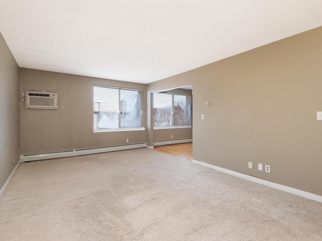 spare room with a baseboard heating unit, an AC wall unit, light colored carpet, and baseboards