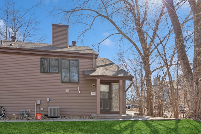 back of house featuring central air condition unit, a chimney, and a yard