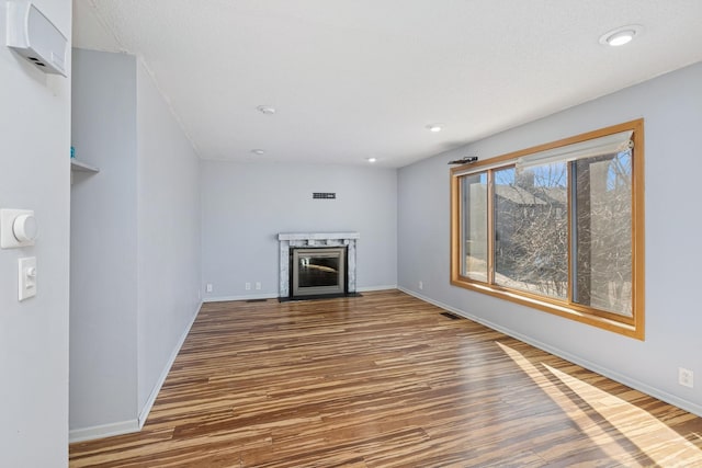 unfurnished living room featuring a premium fireplace, wood finished floors, visible vents, and baseboards