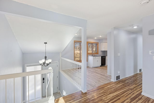 hallway with visible vents, light wood-style flooring, an upstairs landing, a chandelier, and a sink