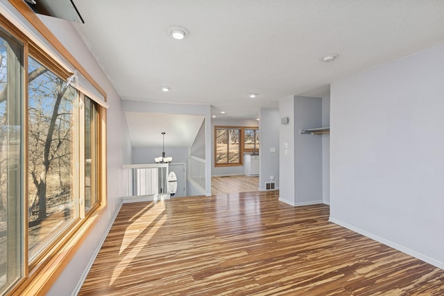 unfurnished room featuring baseboards, wood finished floors, a textured ceiling, a notable chandelier, and recessed lighting