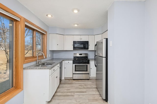 kitchen with stainless steel appliances, white cabinetry, a sink, light stone countertops, and light wood-type flooring