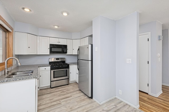 kitchen featuring light wood-style floors, appliances with stainless steel finishes, white cabinets, and a sink