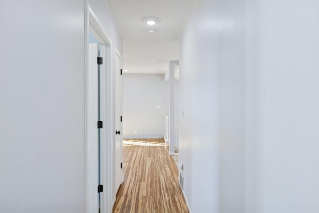 hall featuring a textured ceiling, wood finished floors, and baseboards