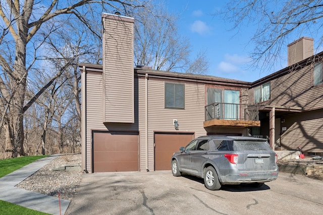 view of home's exterior with an attached garage, a chimney, and aphalt driveway