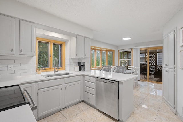 kitchen with a sink, a peninsula, light countertops, and stainless steel dishwasher