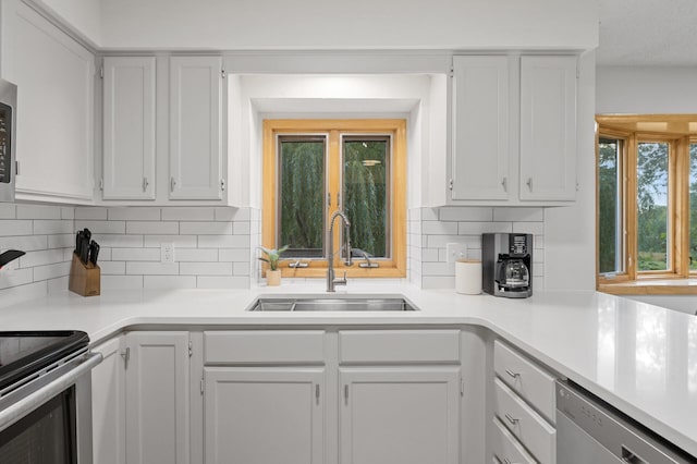 kitchen featuring appliances with stainless steel finishes, white cabinets, light countertops, and a sink