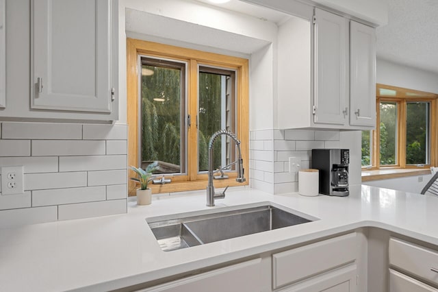 kitchen with light countertops, a sink, backsplash, and white cabinetry