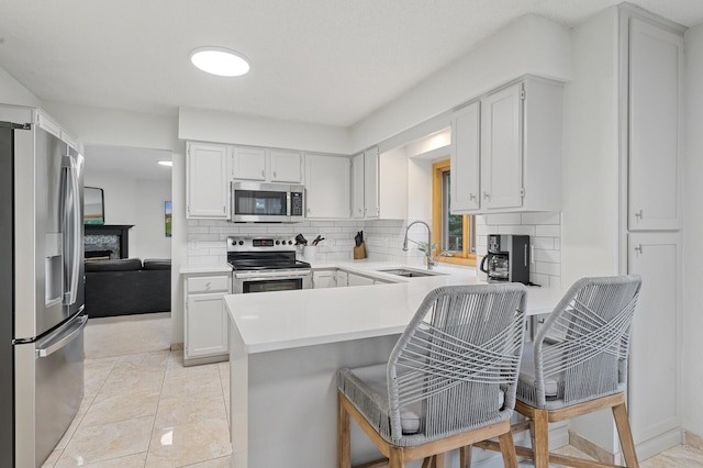 kitchen with a fireplace, stainless steel appliances, a sink, a peninsula, and a kitchen bar